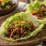 Close-up of ground beef lettuce wraps with carrots, green onions, and sesame seeds served on butter lettuce leaves